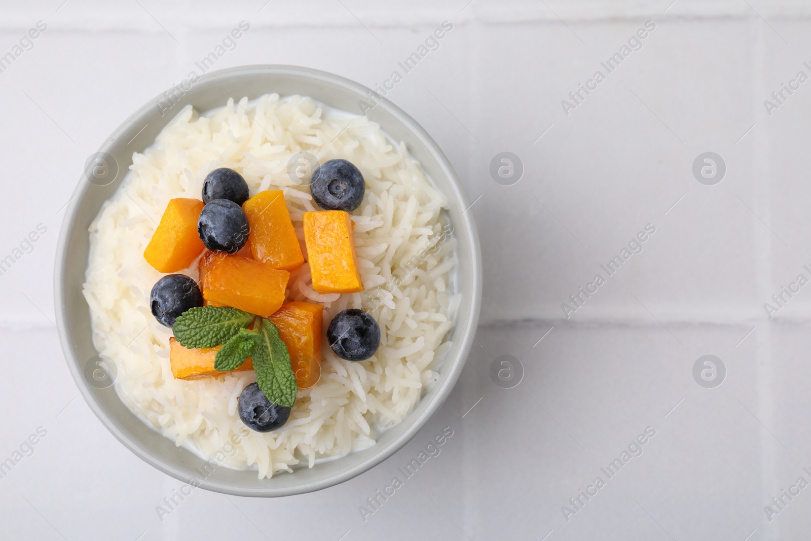 Photo of Bowl of delicious rice porridge with blueberries and pumpkin on white table, top view. Space for text