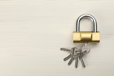 Modern padlock with keys on white wooden table, top view. Space for text