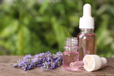 Photo of Bottles with natural lavender essential oil on wooden table against blurred background. Space for text