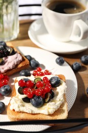 Photo of Cup of coffee near sandwiches with cream cheese and berries on wooden tray