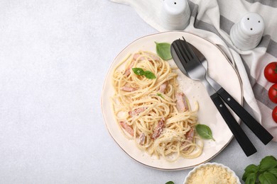 Plate of tasty pasta Carbonara with basil leaves on light grey table, flat lay. Space for text