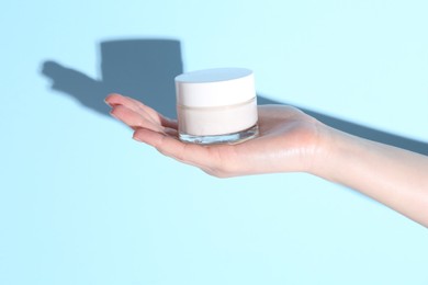 Photo of Woman holding jar of cream on light blue background, closeup