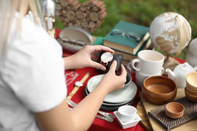 Photo of Woman holding beautiful watch near table with different items on garage sale, closeup