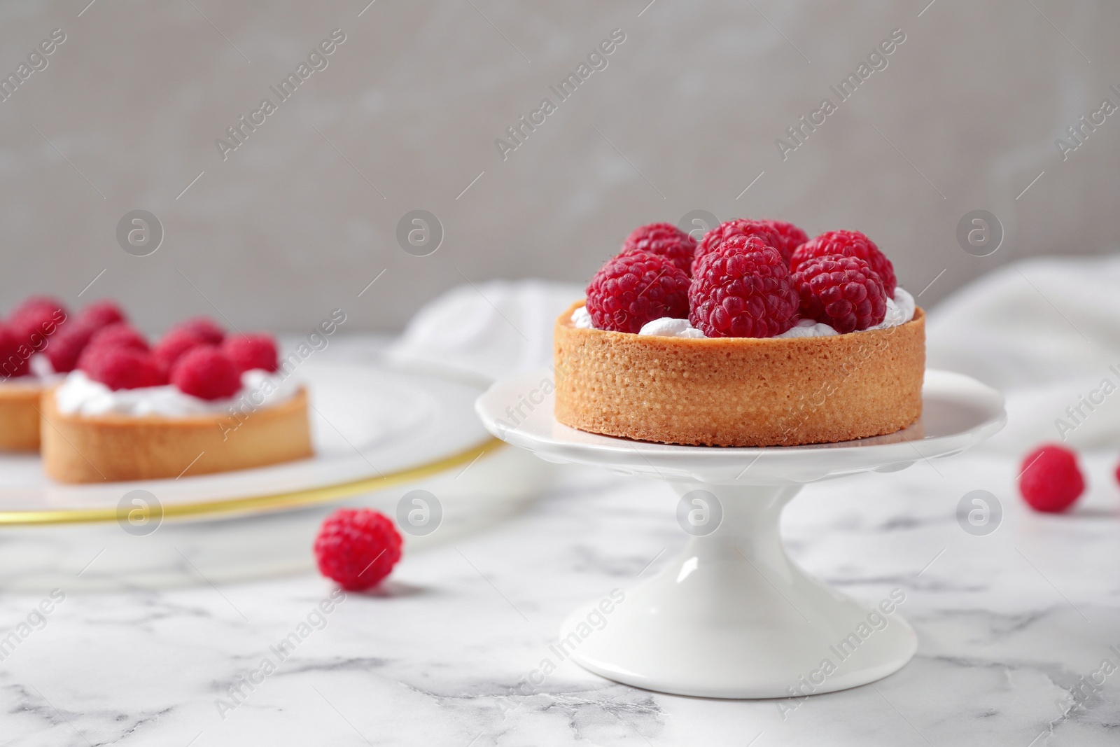 Photo of Cake stand with raspberry tart on marble table against light background. Delicious pastries