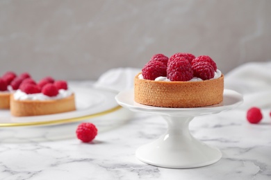 Photo of Cake stand with raspberry tart on marble table against light background. Delicious pastries