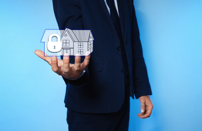 Image of Home security concept. Man holding house on light blue background, closeup