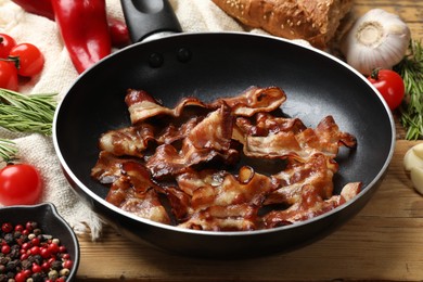 Photo of Delicious bacon slices in frying pan and products on wooden table, closeup