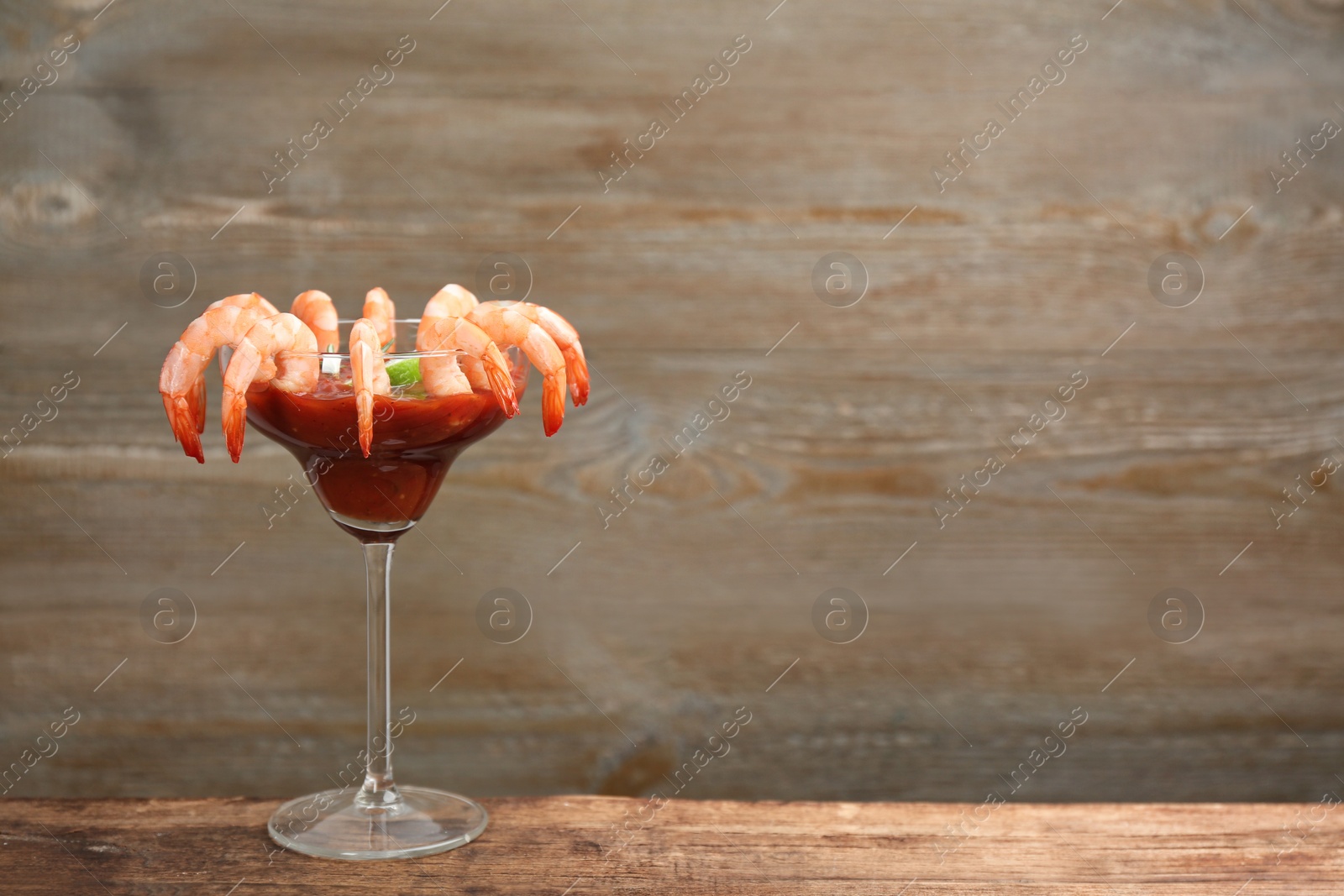 Photo of Shrimp cocktail with tomato sauce on wooden table. Space for text