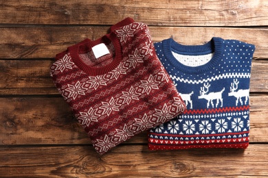 Photo of Christmas sweaters with pattern on wooden background, top view