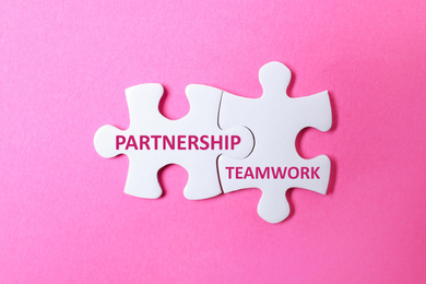 Image of White puzzle pieces with words PARTNERSHIP and TEAMWORK on pink background, top view
