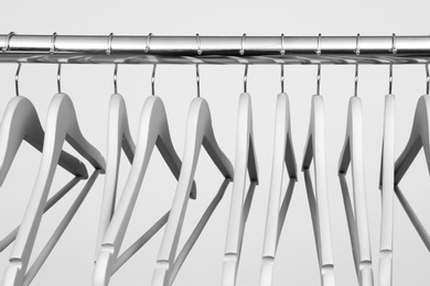 Empty clothes hangers on metal rail against light background, closeup