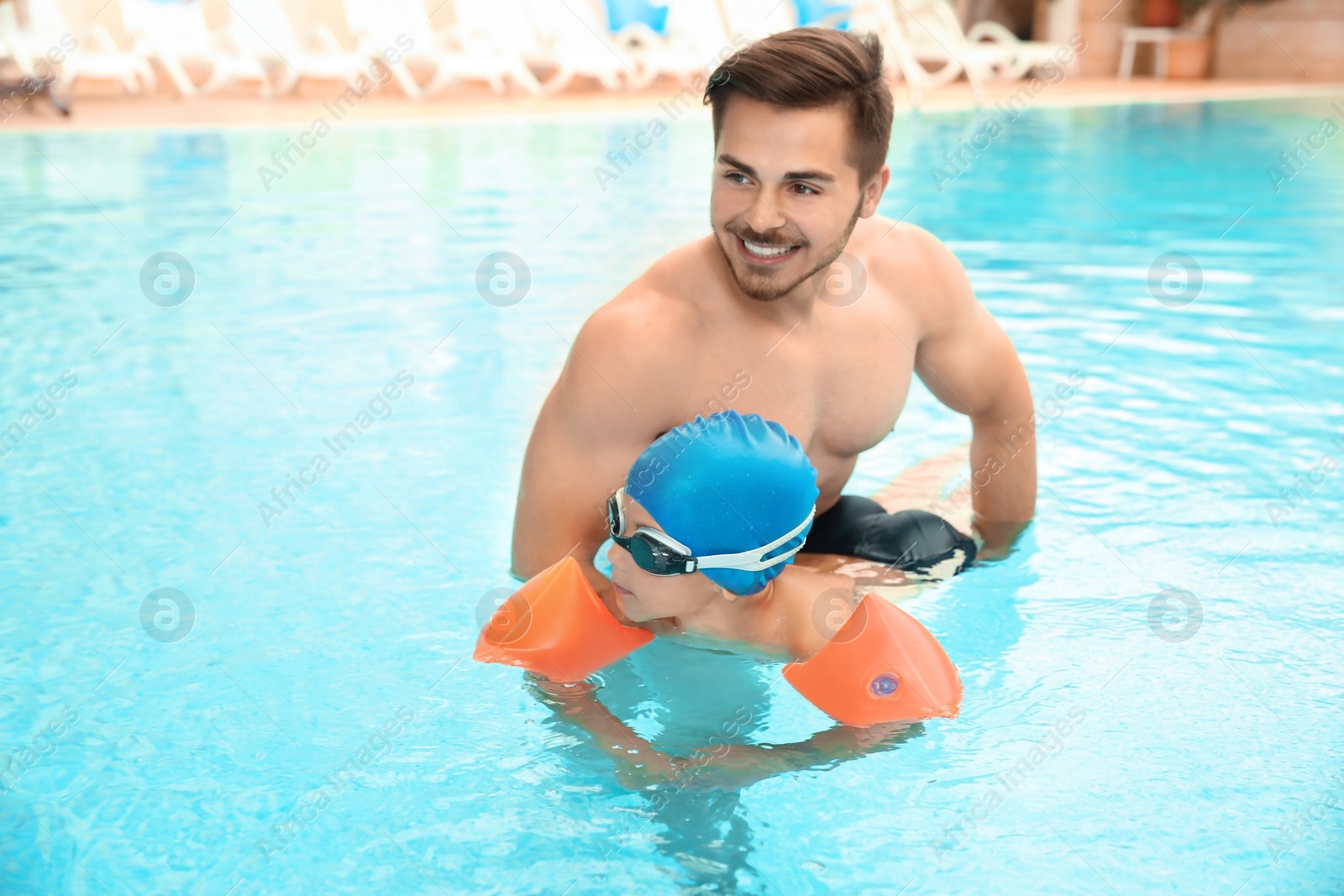 Photo of Happy father teaching his son to swim with inflatable sleeves in pool
