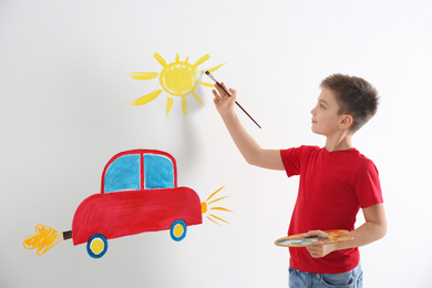 Little child drawing car and sun on white wall indoors