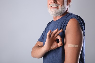 Senior man showing arm with bandage after vaccination on grey background, closeup