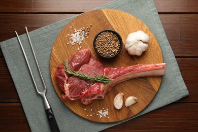 Photo of Raw ribeye steak, spices and fork on wooden table, flat lay