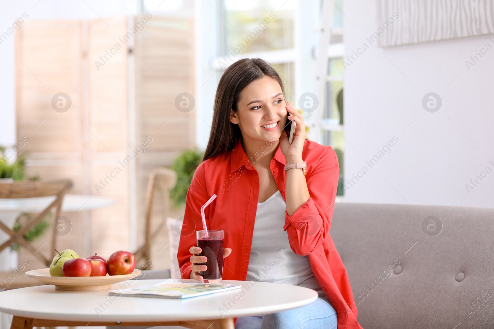 Photo of Young woman using mobile phone while drinking tasty healthy smoothie at table, indoors