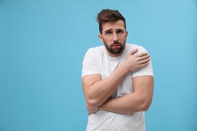 Photo of Man suffering from fever on light blue background, space for text. Cold symptoms