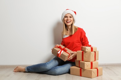 Young woman with Christmas gifts near white wall