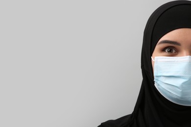 Photo of Muslim woman in hijab and medical mask on light gray background, space for text