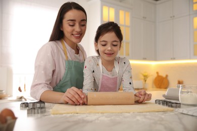 Photo of Mother with her cute little daughter rolling dough in kitchen