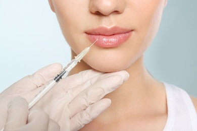 Young woman getting lip injection on color background, closeup