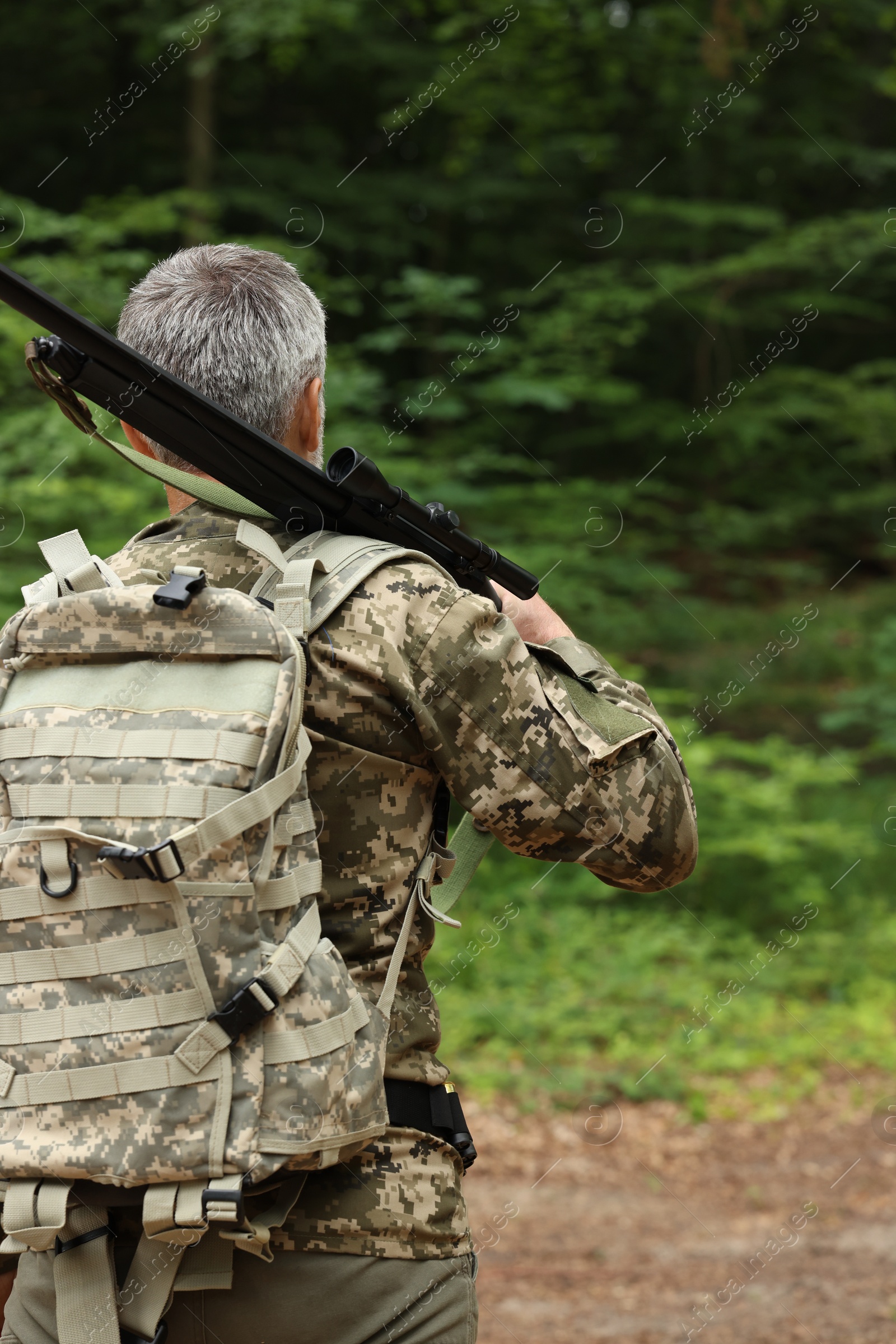 Photo of Man with hunting rifle wearing camouflage in forest, back view