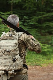 Photo of Man with hunting rifle wearing camouflage in forest, back view