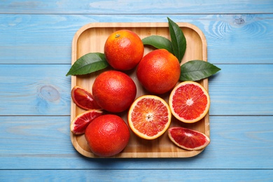 Photo of Whole and cut red oranges with green leaves on light blue wooden table