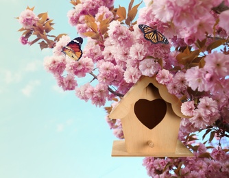 Beautiful wooden bird house hanging on blossoming tree outdoors. Springtime