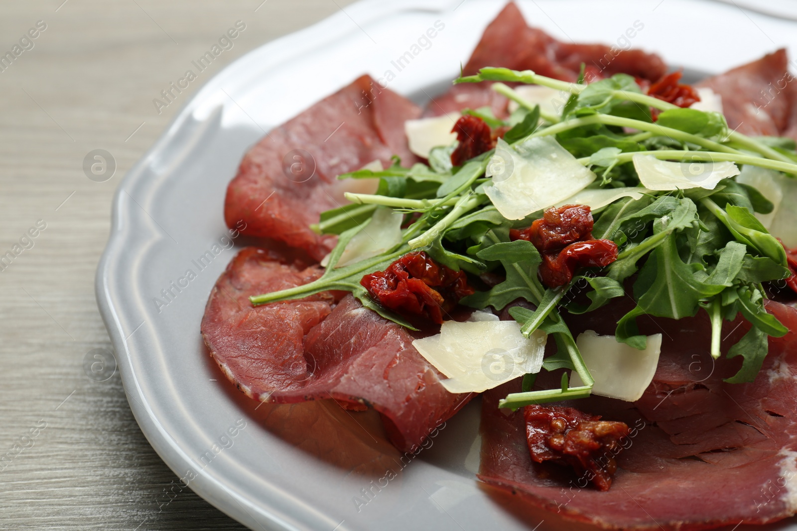 Photo of Plate of tasty bresaola salad with sun-dried tomatoes and parmesan cheese on wooden table, closeup