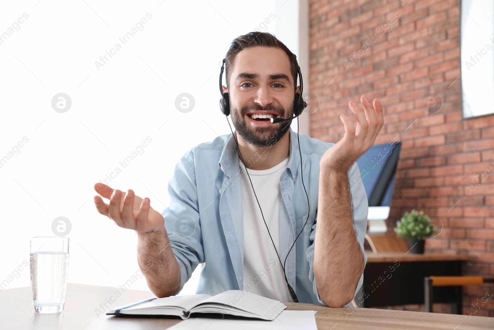 Photo of Young man with headset looking at camera and using video chat in home office