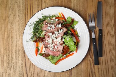 Photo of Delicious salad with roasted meat and vegetables served on wooden table, flat lay