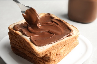 Spreading sweet chocolate cream onto toast on table, closeup