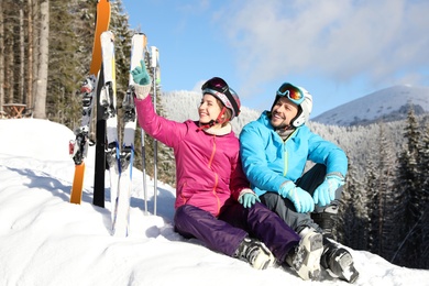 Photo of Happy couple with ski equipment sitting on snow in mountains. Winter vacation