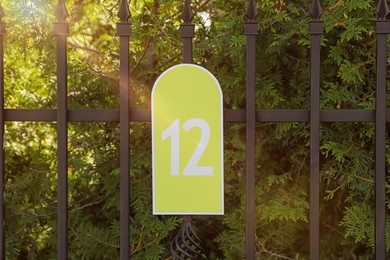 Photo of Plate with house number twelve hanging on iron fence outdoors