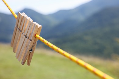 Photo of Wooden clothespins hanging on washing line in mountains, closeup