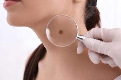 Dermatologist examining patient with magnifying glass in clinic, closeup view