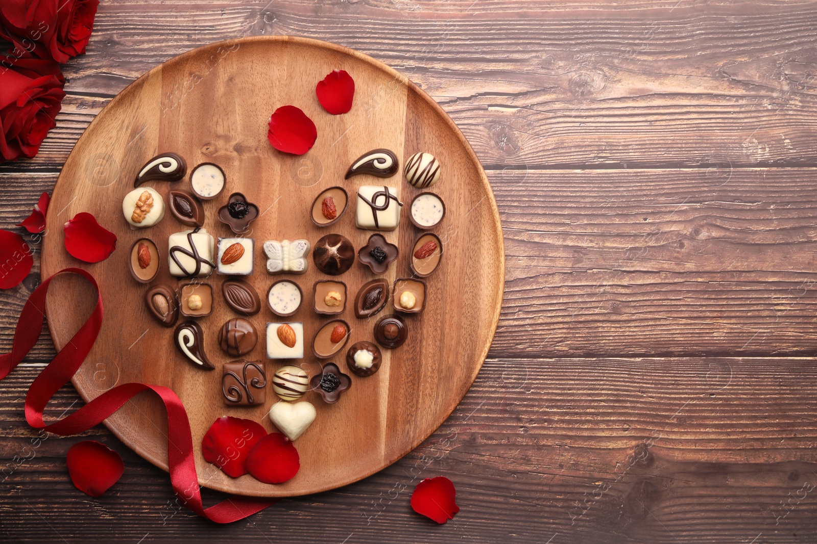 Photo of Heart made with delicious chocolate candies and rose petals on wooden table, top view. Space for text