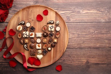 Heart made with delicious chocolate candies and rose petals on wooden table, top view. Space for text