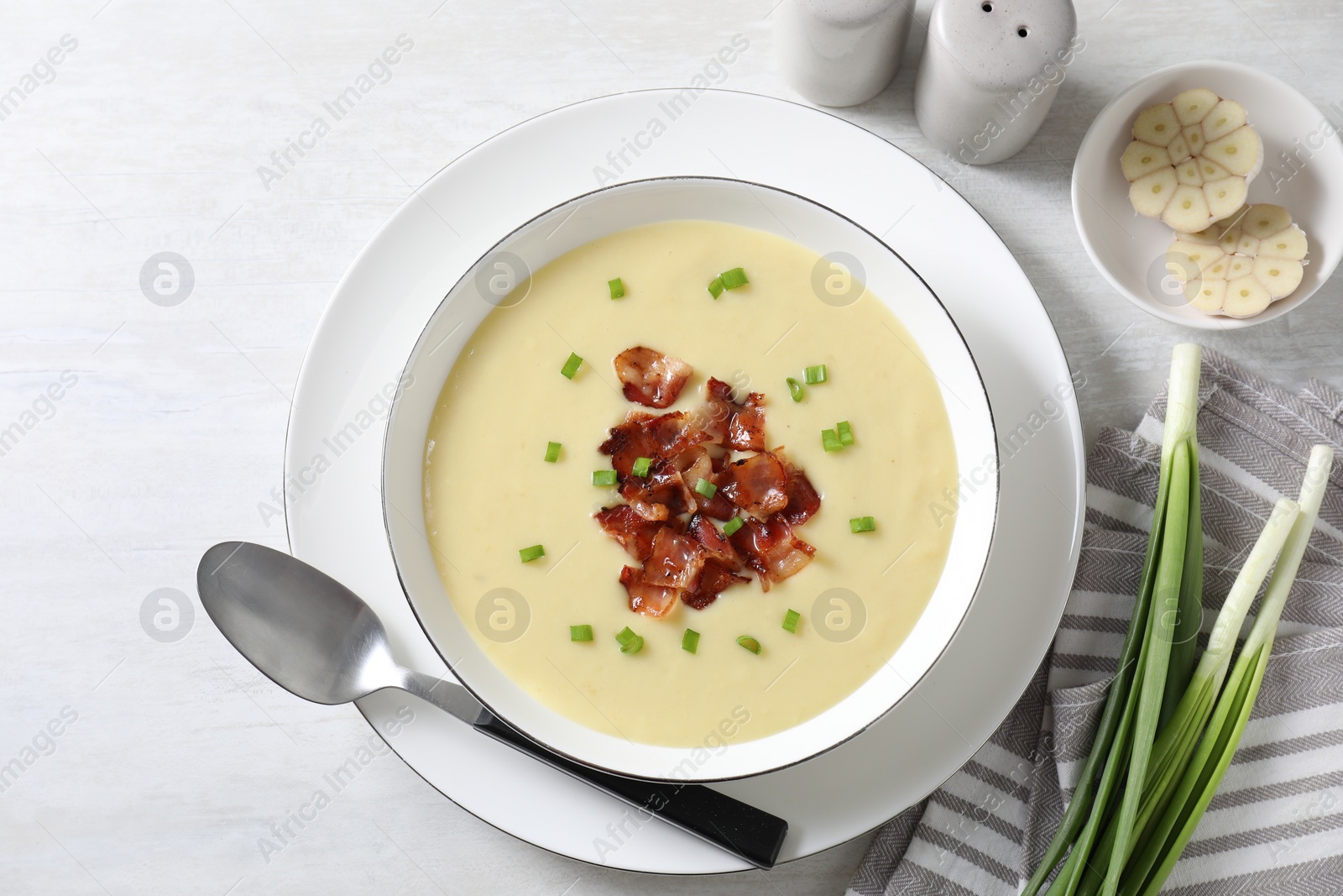 Photo of Tasty potato soup with bacon in bowl served on white wooden table, flat lay