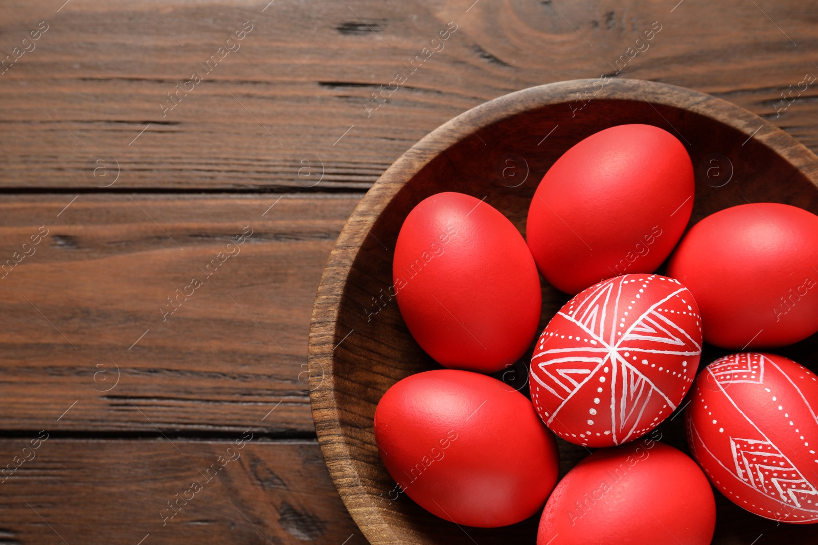 Photo of Wooden bowl with painted red Easter eggs on table, top view. Space for text