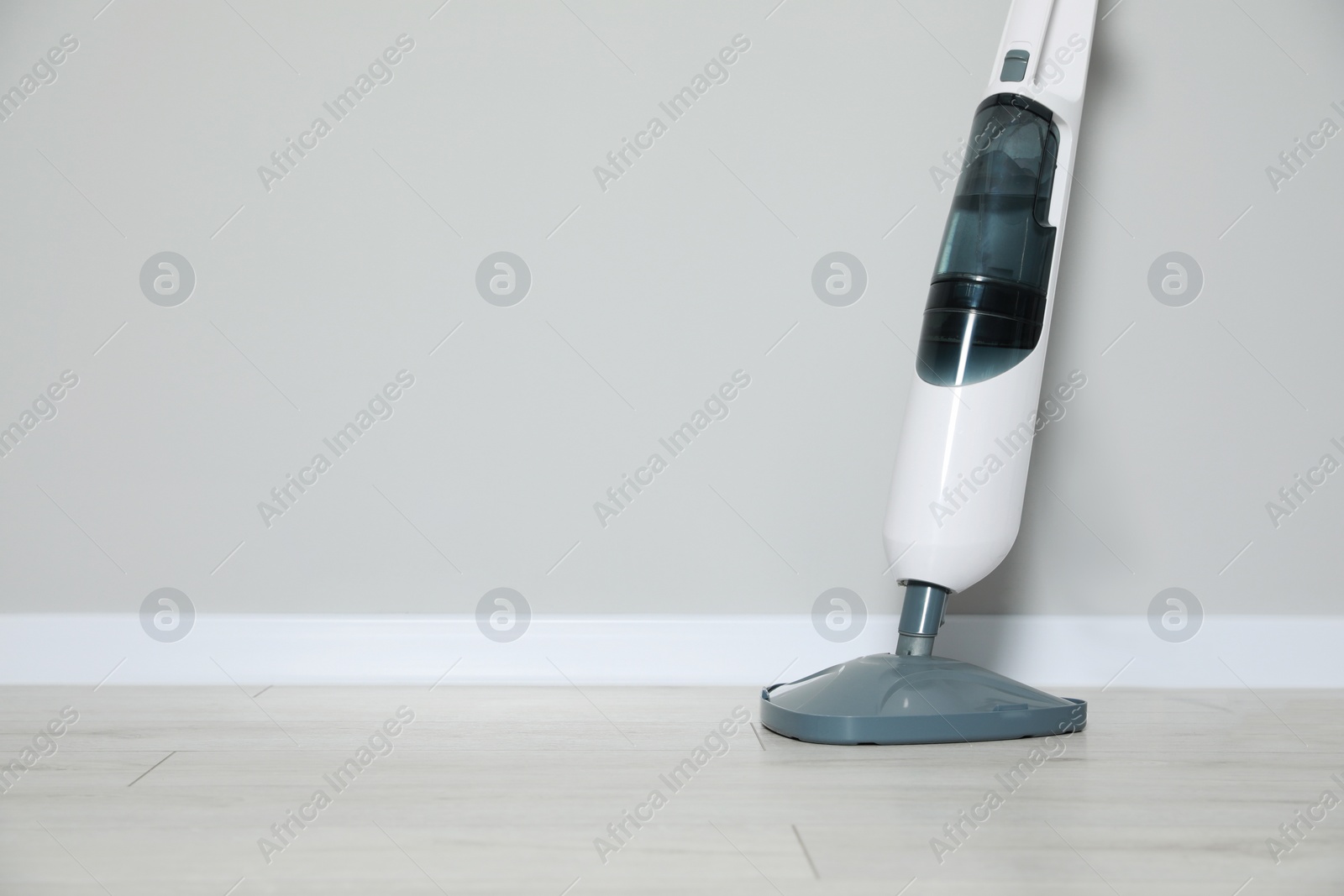 Photo of One modern steam mop on floor near grey wall, space for text