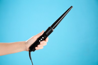 Photo of Woman holding clipless curling hair iron on light blue background, closeup