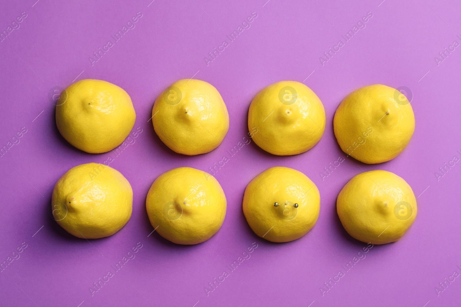 Photo of Cut lemons symbolizing women's breasts and one with nipple piercing on purple background, flat lay