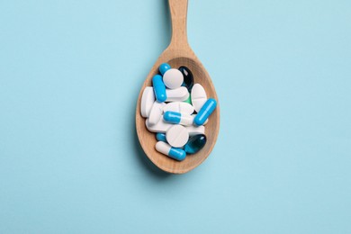 Many different pills in spoon on light blue background, top view
