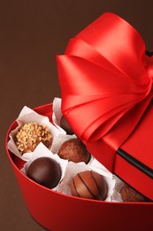 Photo of Heart shaped box with delicious chocolate candies on brown background, closeup