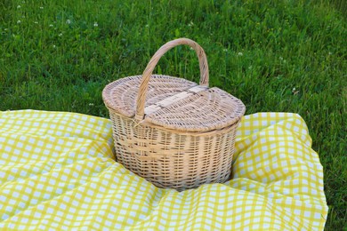 Photo of Picnic basket with checkered tablecloth on green grass outdoors