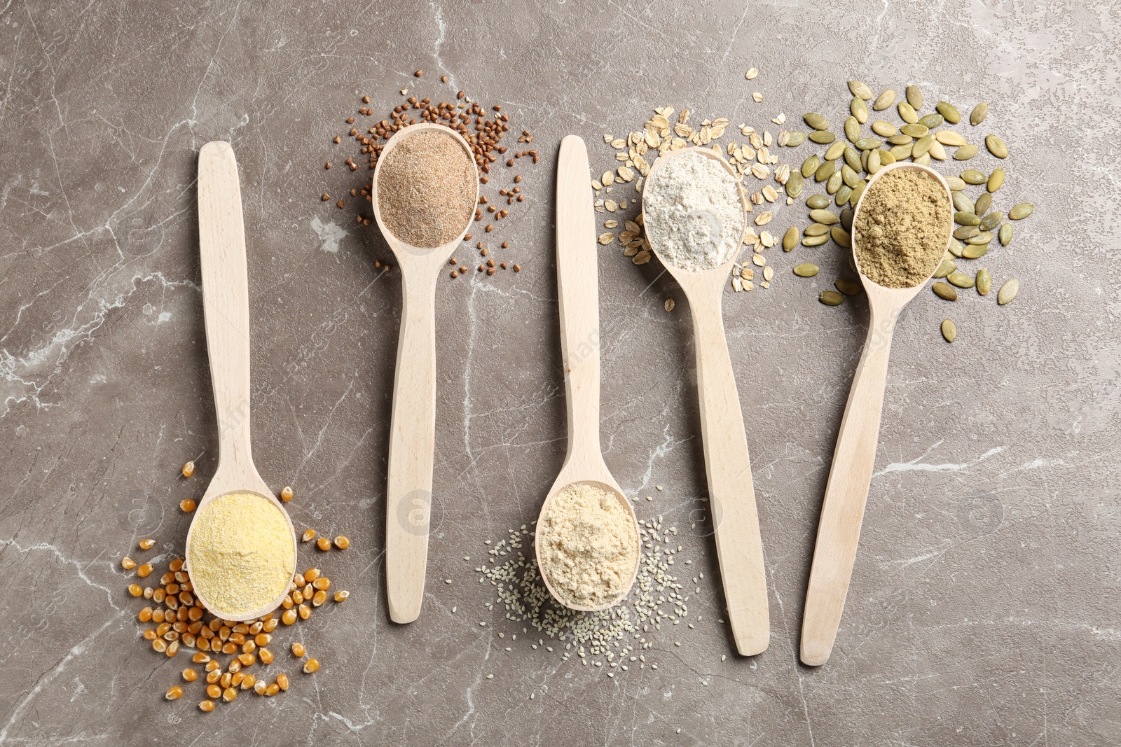 Photo of Spoons with different types of flour and ingredients on table, top view