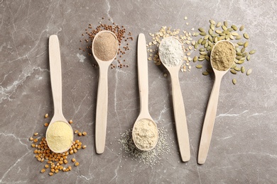 Spoons with different types of flour and ingredients on table, top view