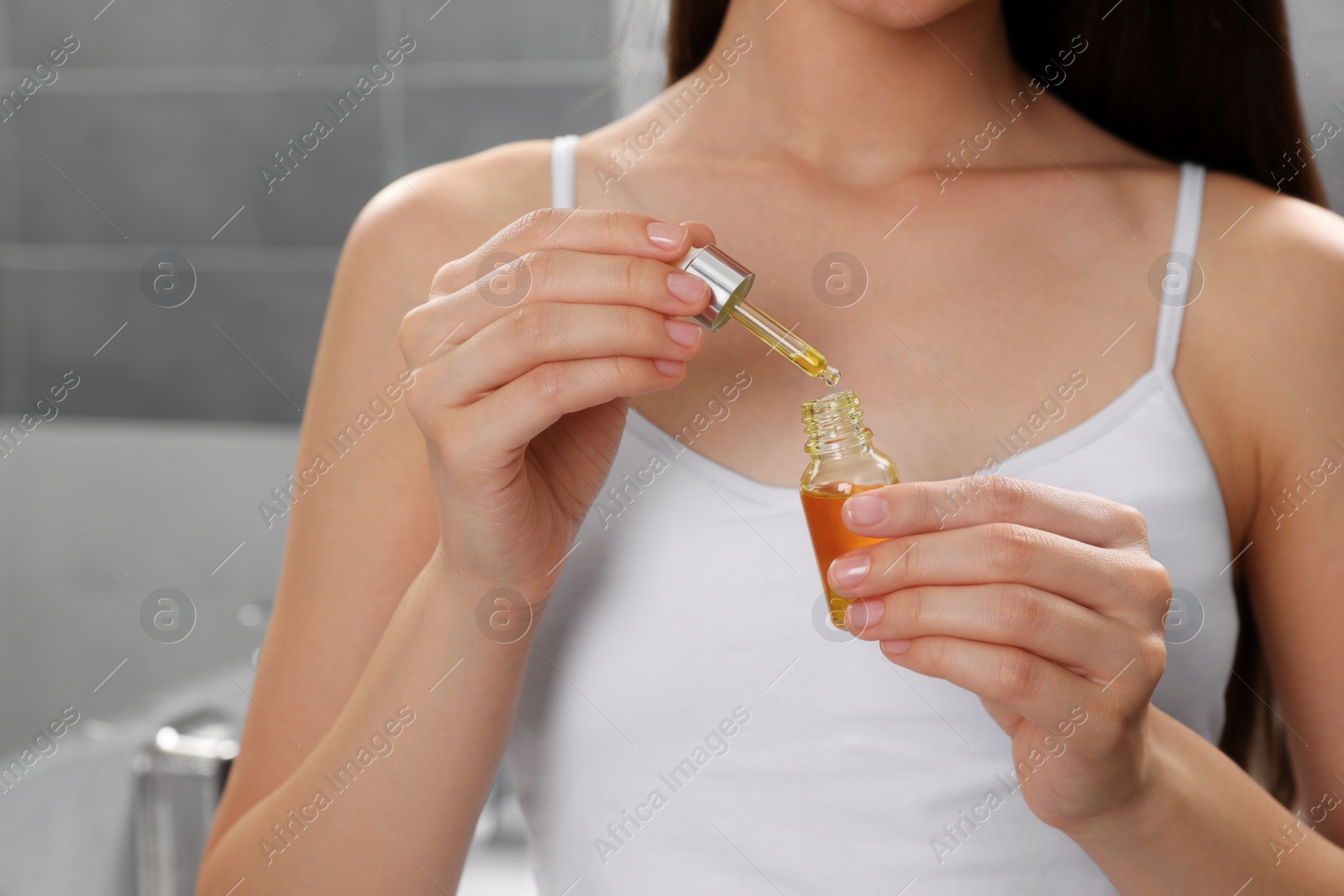 Photo of Young woman with bottle of essential oil in bathroom, closeup